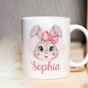 May include: White ceramic mug with a pink and gray bunny illustration. The bunny has a pink bow with white polka dots and the name "Sophia" is written in pink below the bunny.