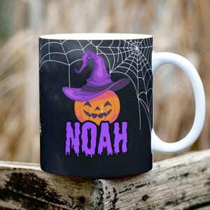 Peut inclure: Mug en céramique blanche avec un fond noir représentant une citrouille portant un chapeau de sorcière violet et un motif de toile d'araignée. Le nom "NOAH" est écrit en lettres violettes qui coulent.