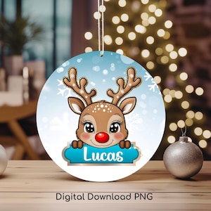 以下が含まれることがあります： 青いバナーに「Lucas」と書かれた、赤い鼻をした漫画のトナカイが描かれた丸いクリスマスオーナメント。オーナメントは、青と白の雪の結晶模様の白い背景です。