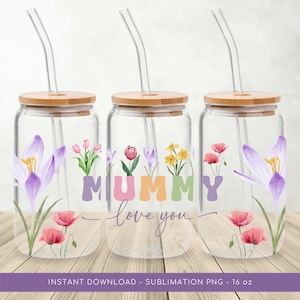 Puede incluir: Tres vasos de vidrio transparentes con tapas de bambú y pajitas. Cada vaso presenta un diseño floral diferente con las palabras "Mamá te quiero" en letras de colores.