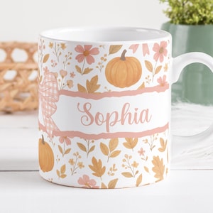 May include: White ceramic mug with a fall-themed design. The mug features pumpkins, flowers, and leaves in shades of orange, pink, and gold. The name "Sophia" is written in a cursive font on a pink banner.