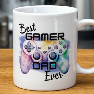 May include: White ceramic mug featuring a colourful watercolour design of a video game controller. The text "Best Gamer Dad Ever" is printed on the mug.