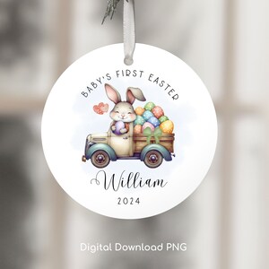 May include: A white round ornament with a bunny carrying a basket of colorful Easter eggs in a blue truck. The text "Baby's First Easter" is written in a circle around the bunny and truck. The name "William" and the year "2024" are written below the truck.