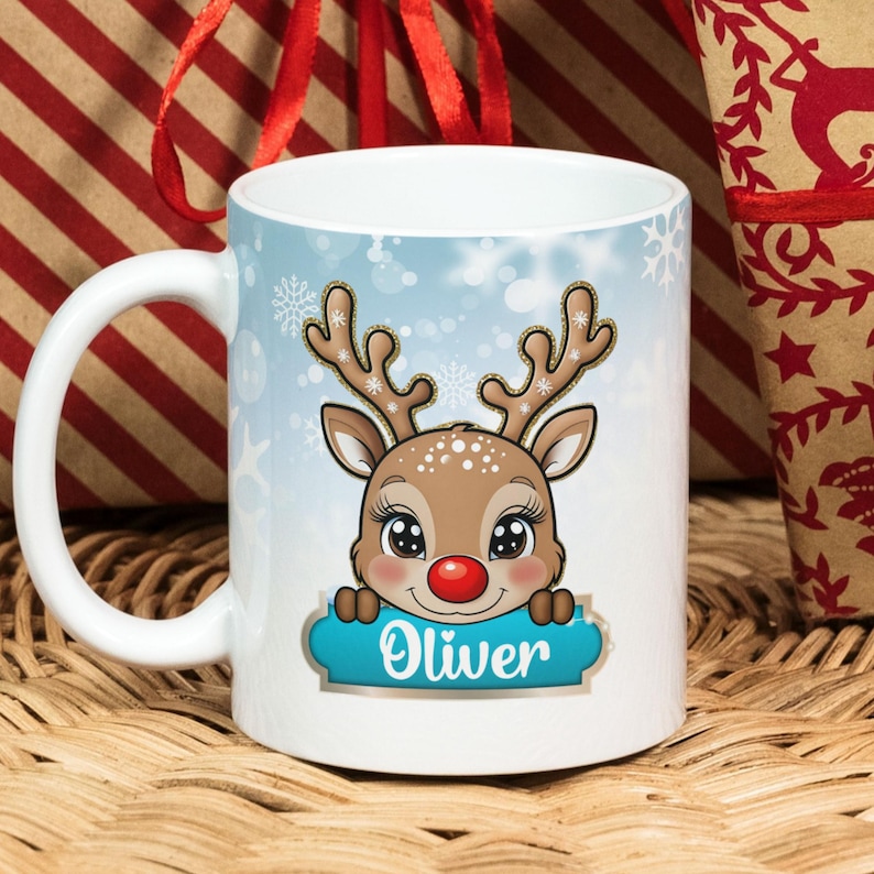 May include: White ceramic mug with a blue and white winter scene featuring a cartoon reindeer with a red nose. The reindeer is peeking over a blue banner with the name "Oliver" written in white.