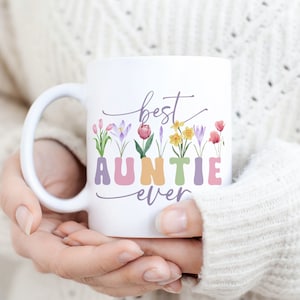 May include: White ceramic mug featuring a floral design and the text "best auntie ever". The letters are in pastel colours and the flowers are in shades of pink, purple, yellow, and green.
