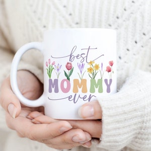 Könnte beinhalten: Weiße Keramiktasse mit Blumenmuster und dem Text "best mommy ever".