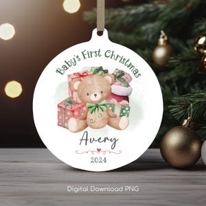 May include: A white round Christmas bauble featuring a watercolour illustration of a teddy bear holding presents. The bauble reads "Baby's First Christmas" and "Avery 2024".