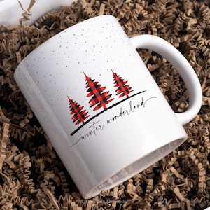 以下が含まれることがあります： 赤と黒の格子縞のクリスマスツリーのデザインと「winter wonderland」の文字が書かれた白いセラミックマグカップです。