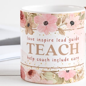 May include: White ceramic mug with a floral design in pink and green. The mug has the words "love inspire lead guide TEACH help coach include care" printed on it.