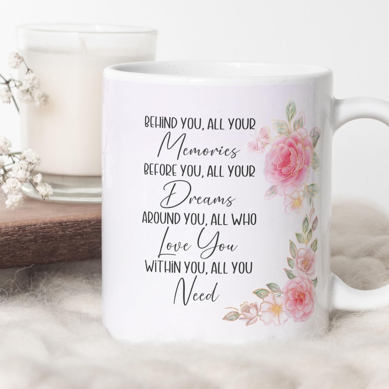 Peut inclure: Un mug en c&eacute;ramique blanche orn&eacute; d'un motif floral de roses roses et de feuilles vertes sur le c&ocirc;t&eacute; droit. Le texte indique : Behind you, all your memories, before you, all your dreams, around you, all who love you, within you, all you need.