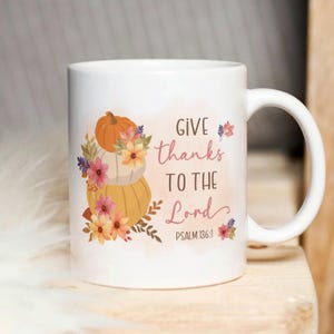 May include: White ceramic coffee mug with a fall-themed design. The mug features a stack of pumpkins with floral accents and the text "Give thanks to the Lord, Psalm 136:1."