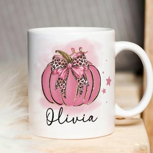 May include: White ceramic mug featuring a pink pumpkin with a leopard print bow and gold glitter. The mug is personalised with the name "Olivia" in black cursive.