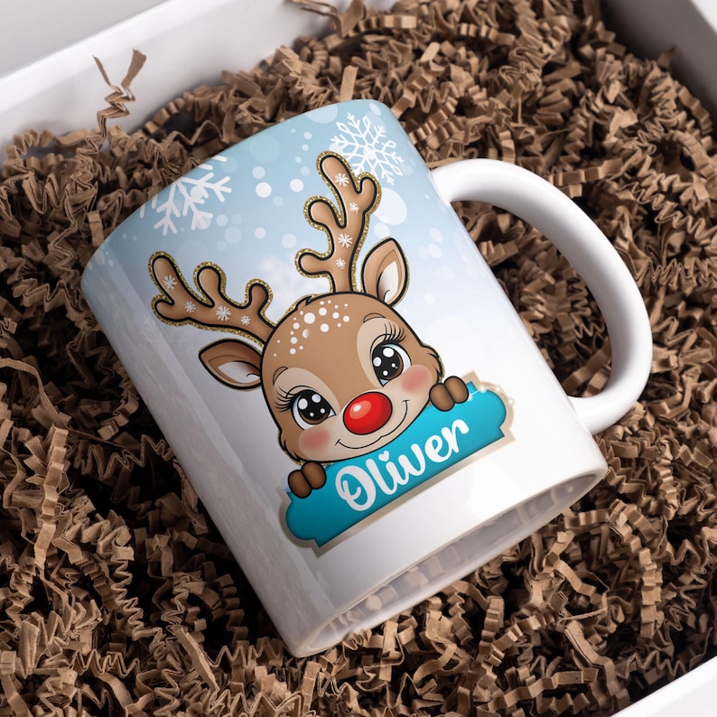 May include: White ceramic mug with a blue and white winter scene featuring a cartoon reindeer with a red nose. The reindeer is holding a blue sign with the name "Oliver" written in gold lettering.