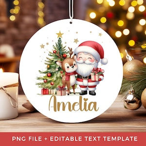 May include: A round white Christmas ornament featuring a cartoon Santa Claus and a reindeer standing next to a decorated pine tree with gold stars. The name Amelia is printed in gold script at the bottom, and the ornament hangs from a white string.