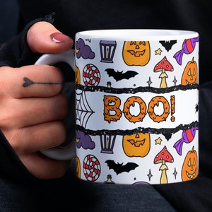 Könnte beinhalten: Weiße Keramiktasse mit Halloween-Motiv. Die Tasse zeigt ein schwarz-weißes Muster aus Fledermäusen, Kürbissen, Süßigkeiten und einem Spinnennetz. Die Worte "BOO!" sind in orangefarbenen und gelben, tropfenden Buchstaben geschrieben.