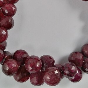 May include: A strand of deep red ruby gemstone beads. The beads are faceted and have a teardrop shape. The beads are strung on a silver thread.