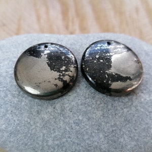 May include: Two round, silver and black pyrite stone pendants with a hole at the top for hanging.