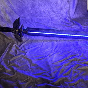 以下が含まれることがあります： 金色の柄と青い光を放つ刃を持つ黒い剣。剣は青い布の表面に置かれている。