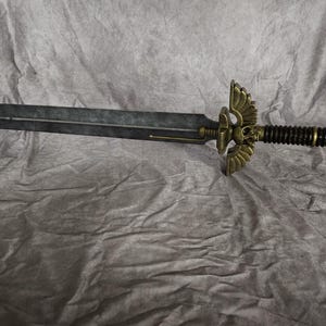 以下が含まれることがあります： 柄に頭蓋骨と翼が付いた黒と金の剣。剣は黒い柄と金の刃を持っている。