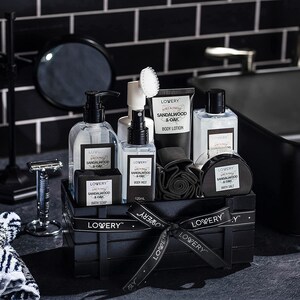 May include: A black wooden crate filled with bath and body products. The products include bottles of body lotion, body mist, bath soap, and bath salt. The products are labeled "Sandalwood & Oak" and are arranged with a black ribbon.