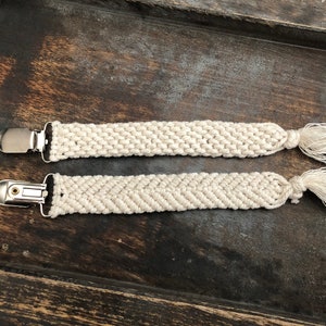 May include: Two white cotton cord straps with metal clips and tassels. The straps are woven in different patterns.