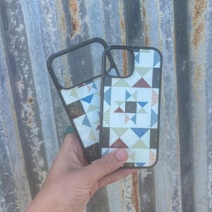 May include: Two black-framed smartphone cases featuring a repeating geometric quilt-inspired pattern. The design consists of small triangles in shades of blue, green, brown, and cream, arranged to form star-like shapes across the back surface.