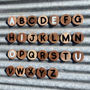 May include: Wooden alphabet letter tiles with white painted letters on a brown background. The letters are arranged in alphabetical order.