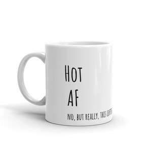 May include: White ceramic coffee mug with black text that reads "HOT AF NO, BUT REALLY, THIS COFFEE IS HOT AF".