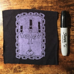 May include: A black fabric patch with a purple image of a candelabra with three candles inside a chain-link frame.