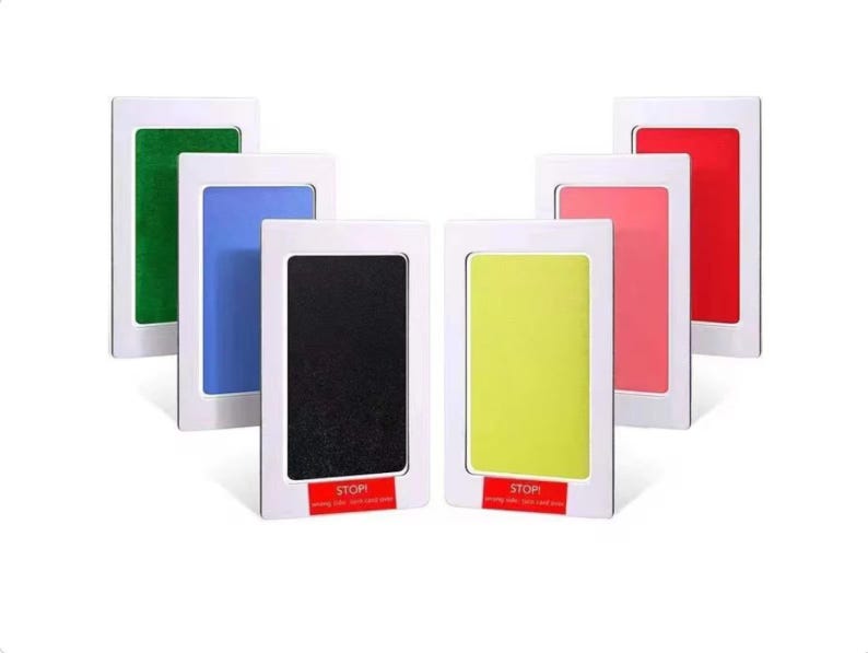 May include: Six ink pads for making baby handprints and footprints. The pads are in white frames with red "STOP" labels. The ink colors are green, blue, black, yellow, pink, and red.