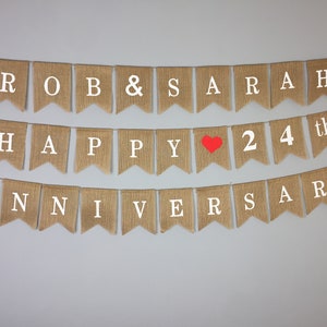 Peut inclure: Une banni&egrave;re en toile de jute avec le texte "ROB & SARAH HAPPY &hearts; 24th ANNIVERSARY" en lettres blanches. Le c&oelig;ur est rouge.