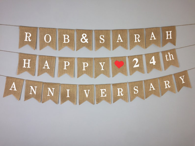 Peut inclure: Une banni&egrave;re en toile de jute avec le texte "ROB & SARAH HAPPY &hearts; 24th ANNIVERSARY" en lettres blanches. Le c&oelig;ur est rouge.