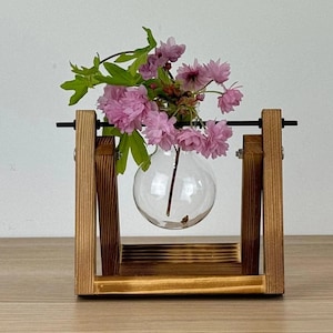May include: A wooden stand with a glass vase holding pink flowers. The stand is made of natural wood and has a rustic look.