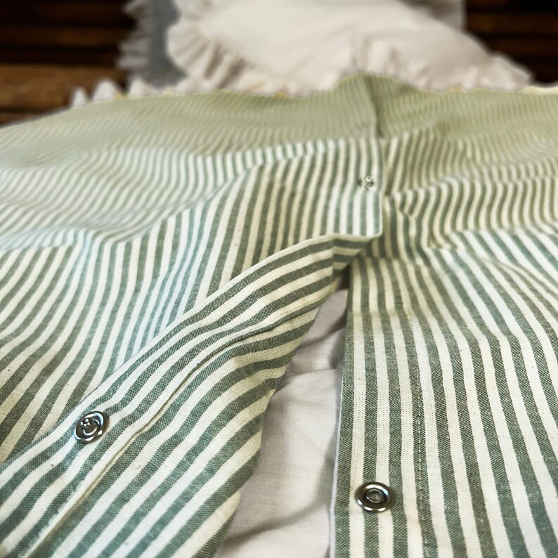 May include: Close-up of a green and white striped fabric with silver buttons. The fabric is folded in half and the buttons are visible on both sides.