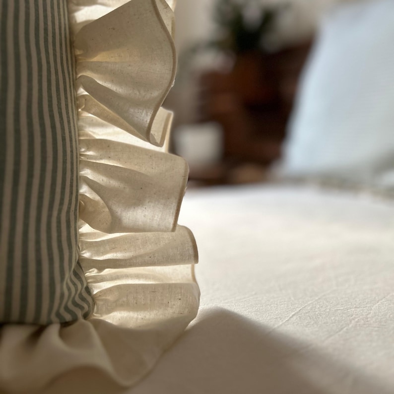 May include: A close-up of a white pillow with a ruffled edge. The pillow is sitting on a white bedspread.