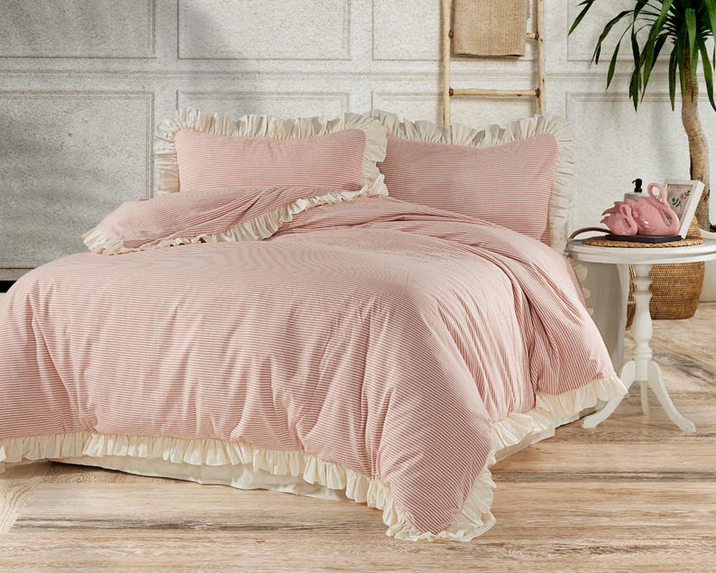 May include: A pink and white striped duvet cover with a ruffled edge. The duvet cover is on a bed with two matching pillowcases.