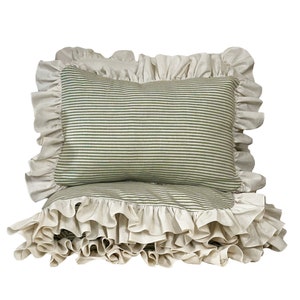 May include: Two pillowcases with a ruffled edge. The pillowcases are made of a white fabric with green stripes. The pillowcases are stacked on top of each other.