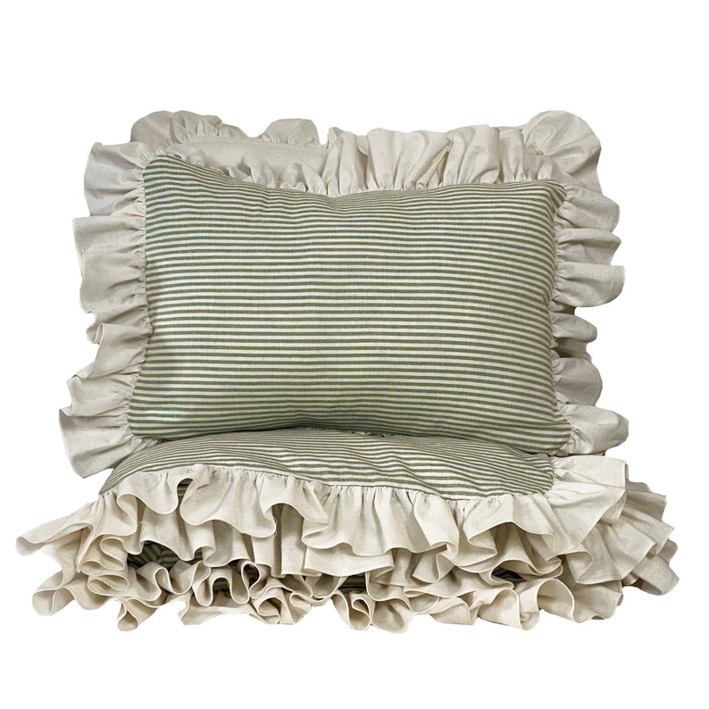 May include: Two pillowcases with a ruffled edge. The pillowcases are made of a white fabric with green stripes. The pillowcases are stacked on top of each other.