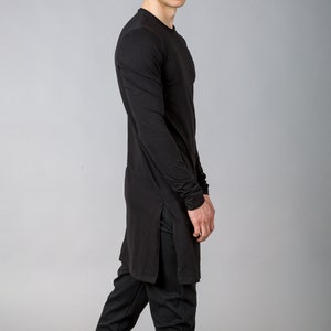 Puede incluir: Una camisa negra de manga larga con una abertura lateral y un corte holgado. La camisa se combina con pantalones negros y zapatillas negras.
