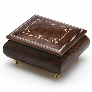 Puede incluir: Una caja de m&uacute;sica de madera con un acabado marr&oacute;n y un dise&ntilde;o floral de incrustaciones en la tapa. La caja de m&uacute;sica tiene patas doradas.