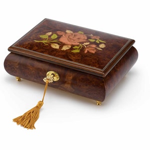May include: A wooden music box with a floral inlay design. The box has a keyhole and a tassel. The box is closed.