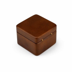 May include: A small, square wooden box with a hinged lid. The box is a dark brown color and has a slightly distressed finish. The lid has two small gold hinges.