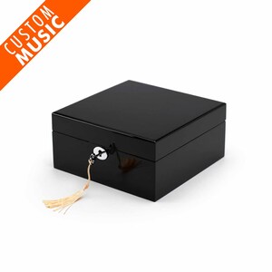 Può includere: Una scatola di legno nera con un lucchetto e una chiave, e un fiocco. La scatola è chiusa.