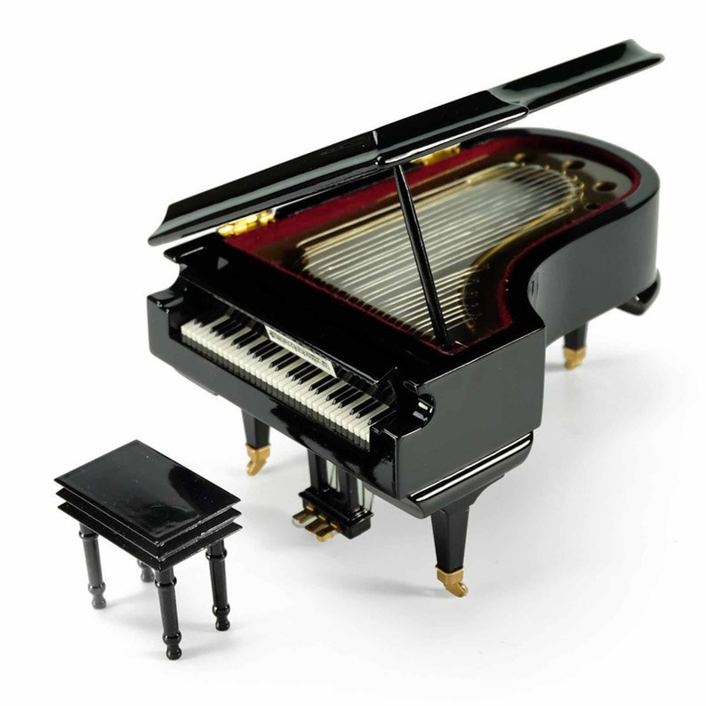 Pode incluir: Um piano de cauda preto com um interior vermelho e um banquinho de piano preto correspondente. O piano tem uma guarni&ccedil;&atilde;o dourada e um conjunto de teclas brancas.