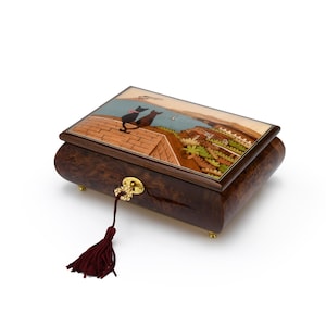 Puede incluir: Una caja de m&uacute;sica de madera con una escena pintada a mano de dos gatos en una azotea con vistas a una ciudad. La caja tiene una cerradura y un borla.