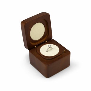 May include: A wooden ring box with a hinged lid, open to reveal a velvet interior with a diamond engagement ring.