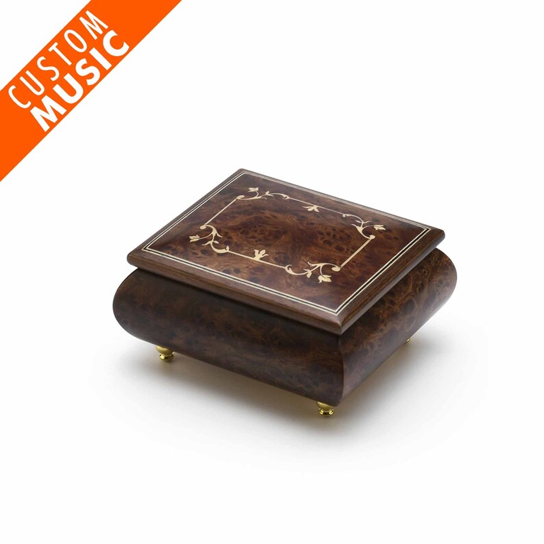 Puede incluir: Una caja de m&uacute;sica de madera con un acabado marr&oacute;n y un dise&ntilde;o floral de incrustaciones en la tapa. La caja de m&uacute;sica tiene patas doradas.