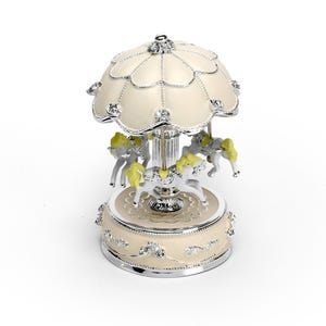 May include: A white and silver carousel music box with three horses. The horses have yellow manes and tails. The carousel has a white roof with silver trim.