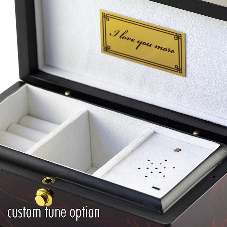 Puede incluir: Caja de m&uacute;sica de madera negra con interior de terciopelo blanco. La caja tiene un peque&ntilde;o compartimento con dos rollos para anillos y un altavoz. La tapa tiene una placa dorada con la inscripci&oacute;n "Te quiero m&aacute;s".