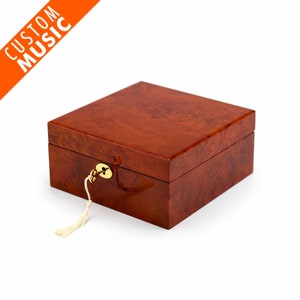 May include: A wooden box with a brown woodgrain finish and a brass lock and key. The box has a tassel attached to the key.